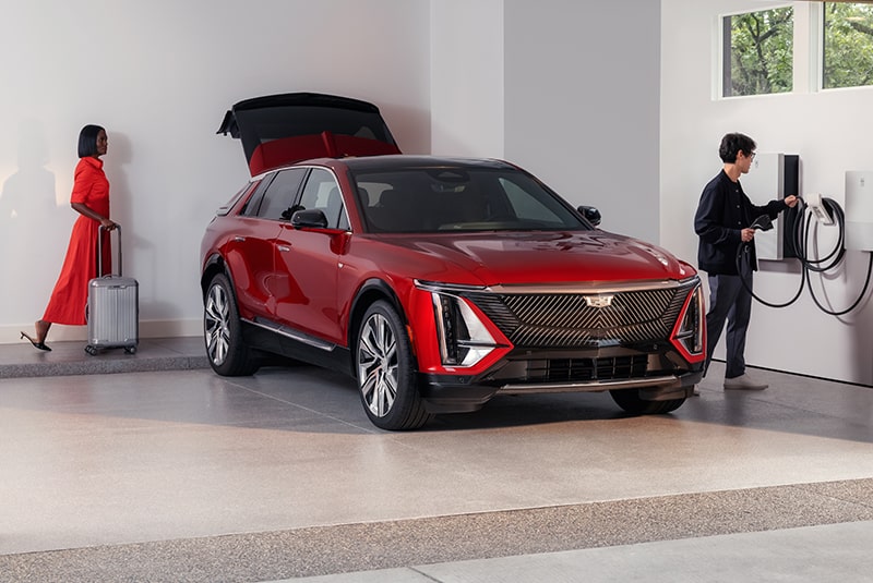 A Man Is Charging a Red Cadillac EV While a Woman is Putting the Luggage in the Trunk