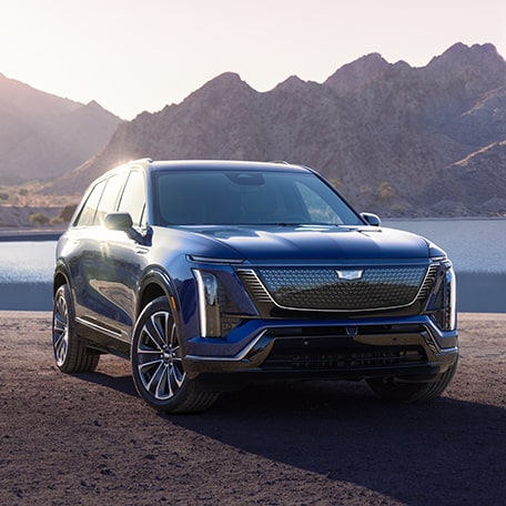 Three Quarters View of a Blue Cadillac Vehicle with a Beautiful Body of Water and Mountain in the Background