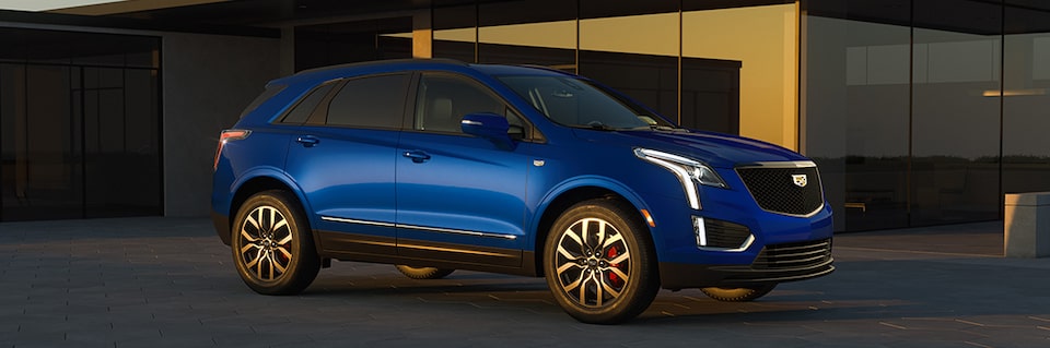 Three-quarters Passenger Side View of the a Blue 2025 Cadillac XT5 Parked Outside an Industrial Building