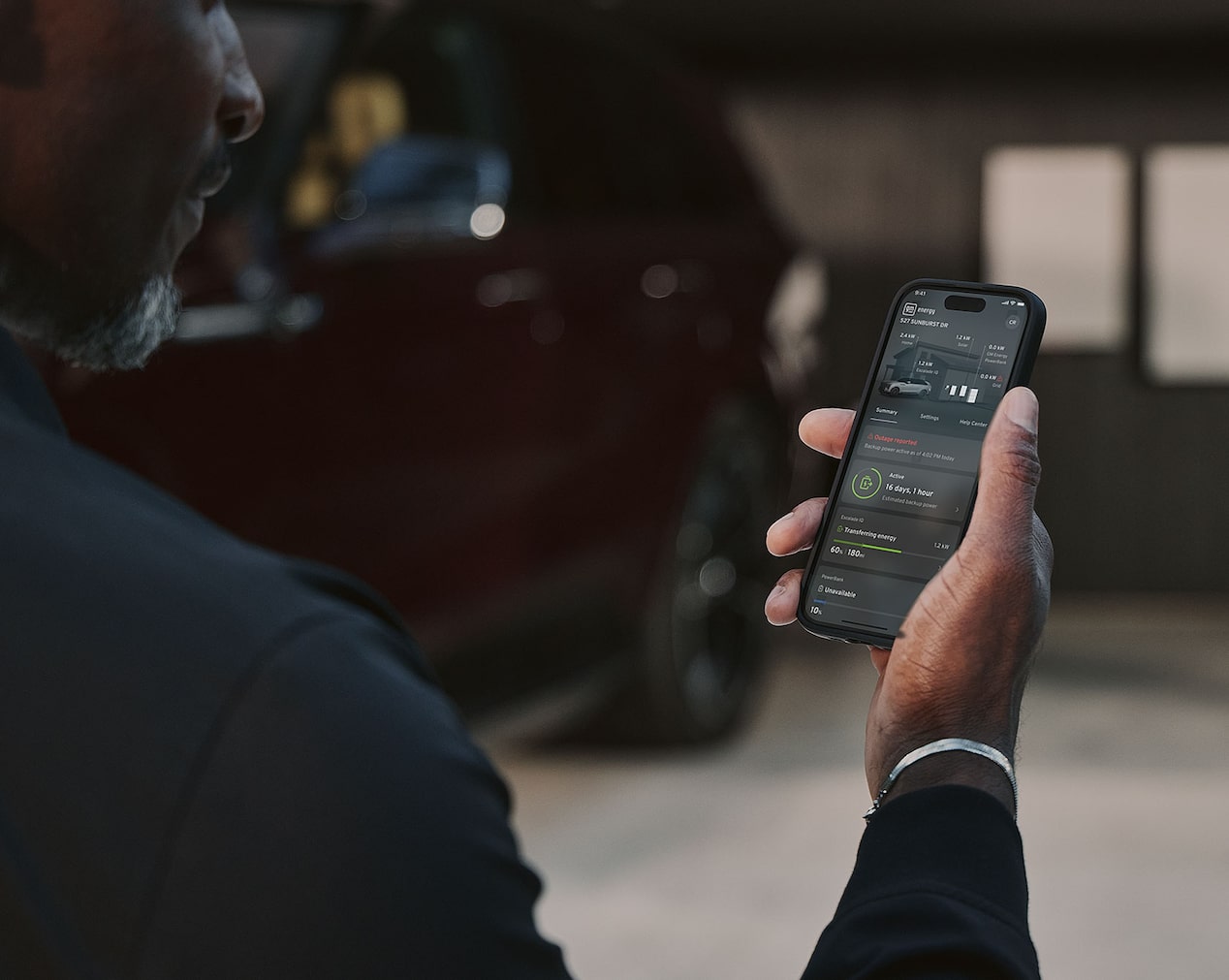 Close-up of a Man Holding a Phone and Looking at the myCadillac App near an Electric Cadillac Vehicle