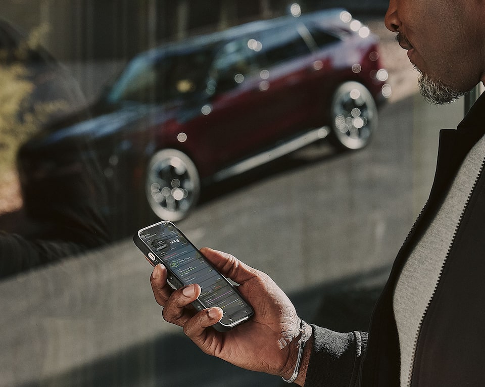 Close-up of a Man Holding a Phone and Looking at the myCadillac App near a Parked Electric Cadillac Vehicle