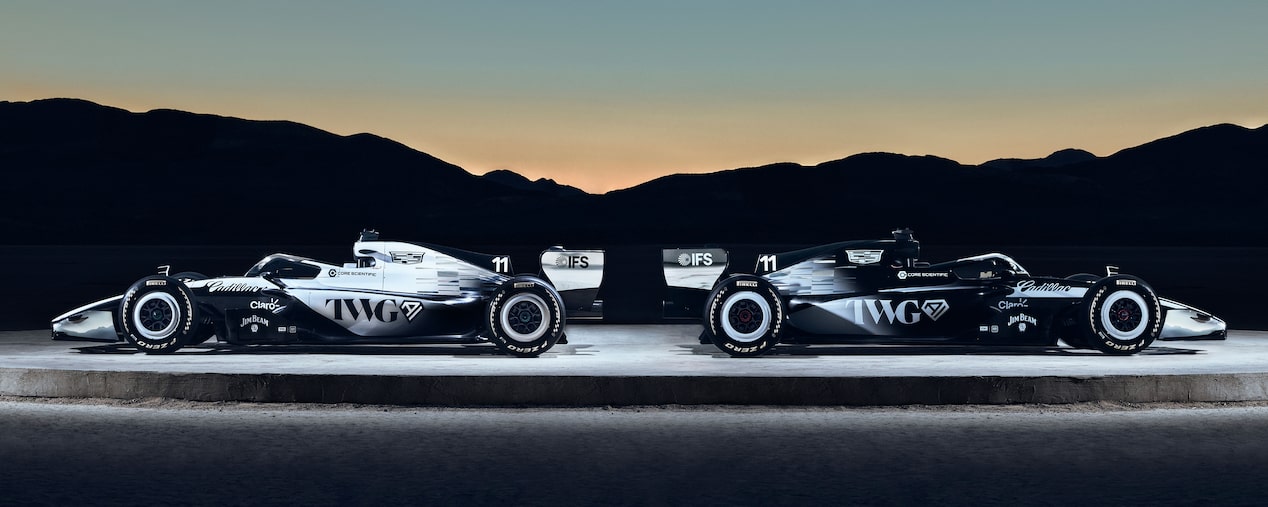 Two Cadillac Racing Cars Facing Outwards on a Circular Structure Outside in the Evening.