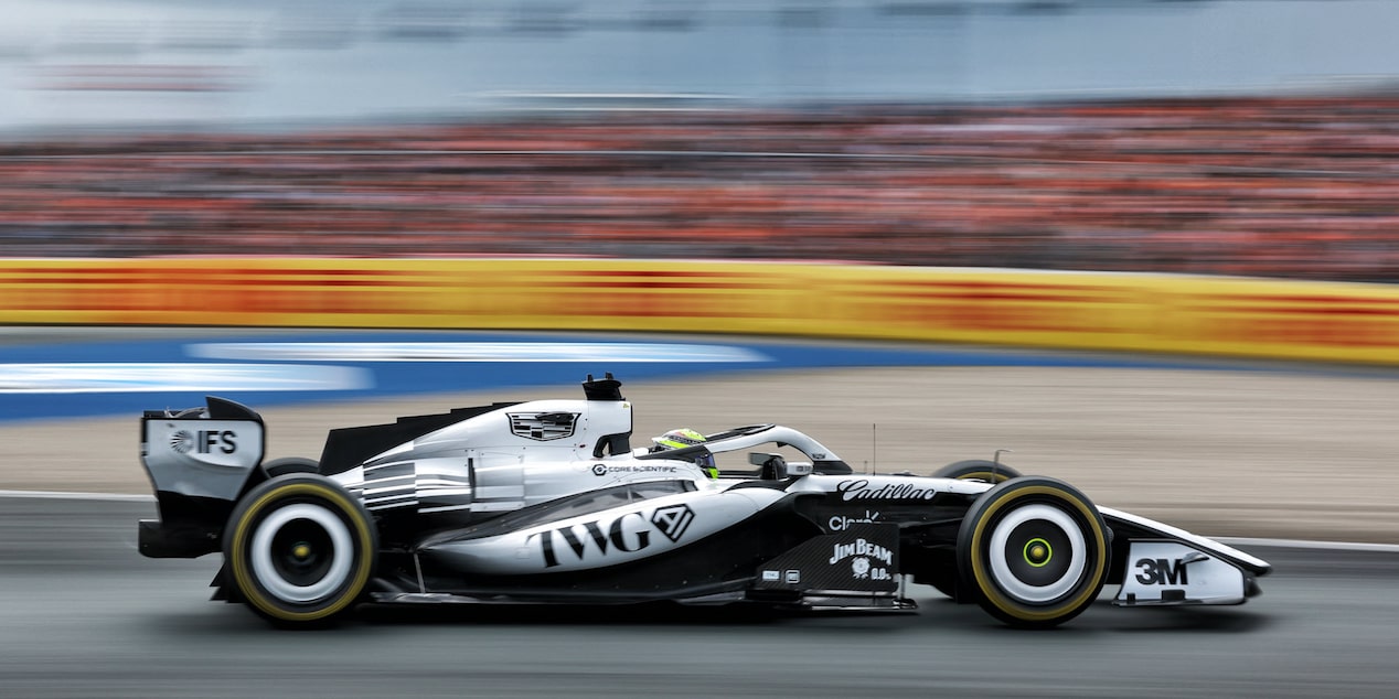 El auto de carrera Cadillac F1 de rines descubiertos avanza a toda velocidad por la pista durante la sesión de práctica. Desenfoque de movimiento de la multitud en el fondo.