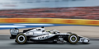 El auto de carrera Cadillac F1 de rines descubiertos avanza a toda velocidad por la pista durante la sesión de práctica. Desenfoque de movimiento de la multitud en el fondo.