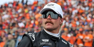 Valtteri Bottas con una gorra blanca del equipo Cadillac Formula 1, de pie en la parrilla antes de la sesión de clasificación, con anteojos de sol y mirando a lo lejos. Una multitud vestida de naranja aparece borrosa detrás de él.