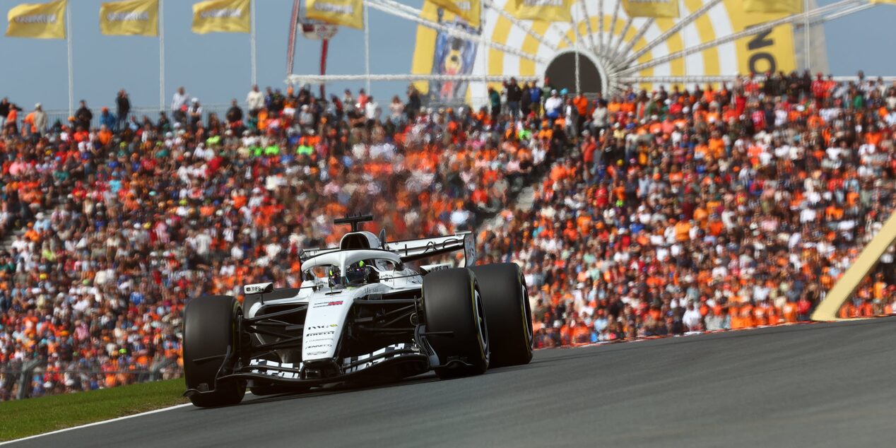 Sergio "Checo" Pérez conduciendo en la pista durante la sesión de clasificación, con una multitud de aficionados vestidos de naranja en las gradas y la rueda de la fortuna detrás de él.