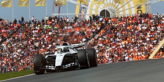 Sergio "Checo" Pérez conduciendo en la pista durante la sesión de clasificación, con una multitud de aficionados vestidos de naranja en las gradas y la rueda de la fortuna detrás de él.