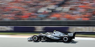 El auto de carrera Cadillac F1 de rines descubiertos avanza a toda velocidad por la pista durante la sesión de clasificación. Desenfoque de movimiento de la multitud en el fondo.