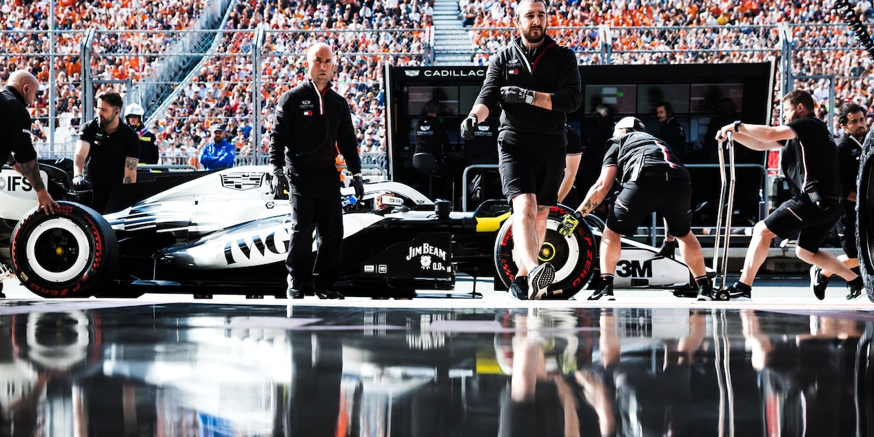 Vista artística del Cadillac F1 en los boxes fuera del garaje del equipo. Reflejo de los ingenieros y del vehículo visible en el suelo debajo de ellos.