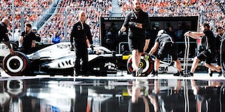 Vista artística del Cadillac F1 en los boxes fuera del garaje del equipo. Reflejo de los ingenieros y del vehículo visible en el suelo debajo de ellos.