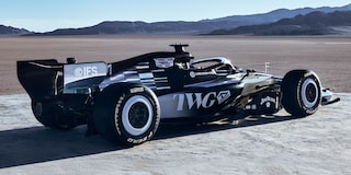 A Sleek Black-And-White Formula Race Car With Prominent Cadillac Branding Parked On A Sunlit Desert Flat With Mountains In the Distance.