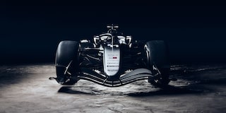 A Low Front View Of A Cadillac-Branded Formula Race Car Illuminated Dramatically Against a Dark Desert Landscape.
