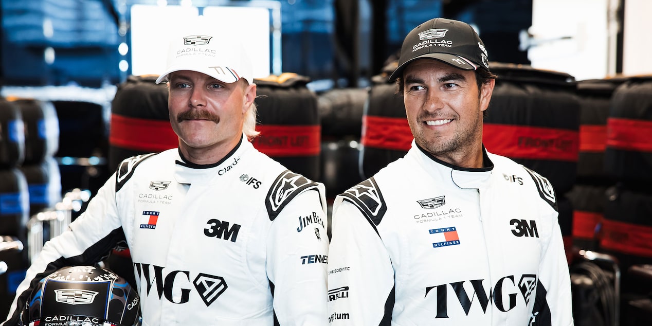Valtteri Bottas And Sergio "Checo" Perez Posing For Photo While Wearing White Firesuits In Team Garage.