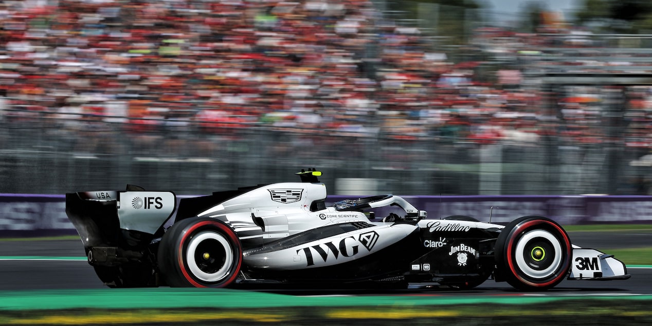 Open-Wheel F1 Cadillac Race Car Speeds Down Racetrack During Practice Session. Motion Blur Of Crowd In The Background.