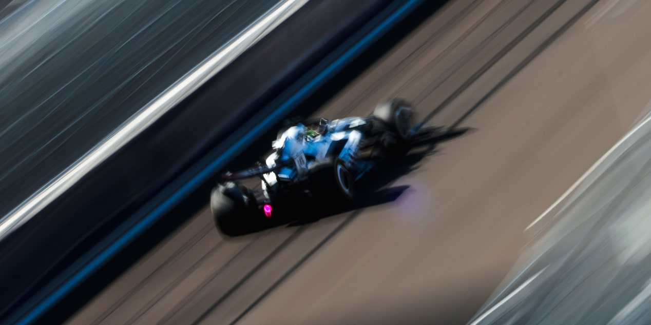 El auto de carrera Cadillac F1 de rines descubiertos avanza a toda velocidad por la pista durante la sesión de práctica. Desenfoque de movimiento de la multitud en el fondo.