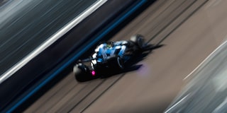 El auto de carrera Cadillac F1 de rines descubiertos avanza a toda velocidad por la pista durante la sesión de práctica. Desenfoque de movimiento de la multitud en el fondo.