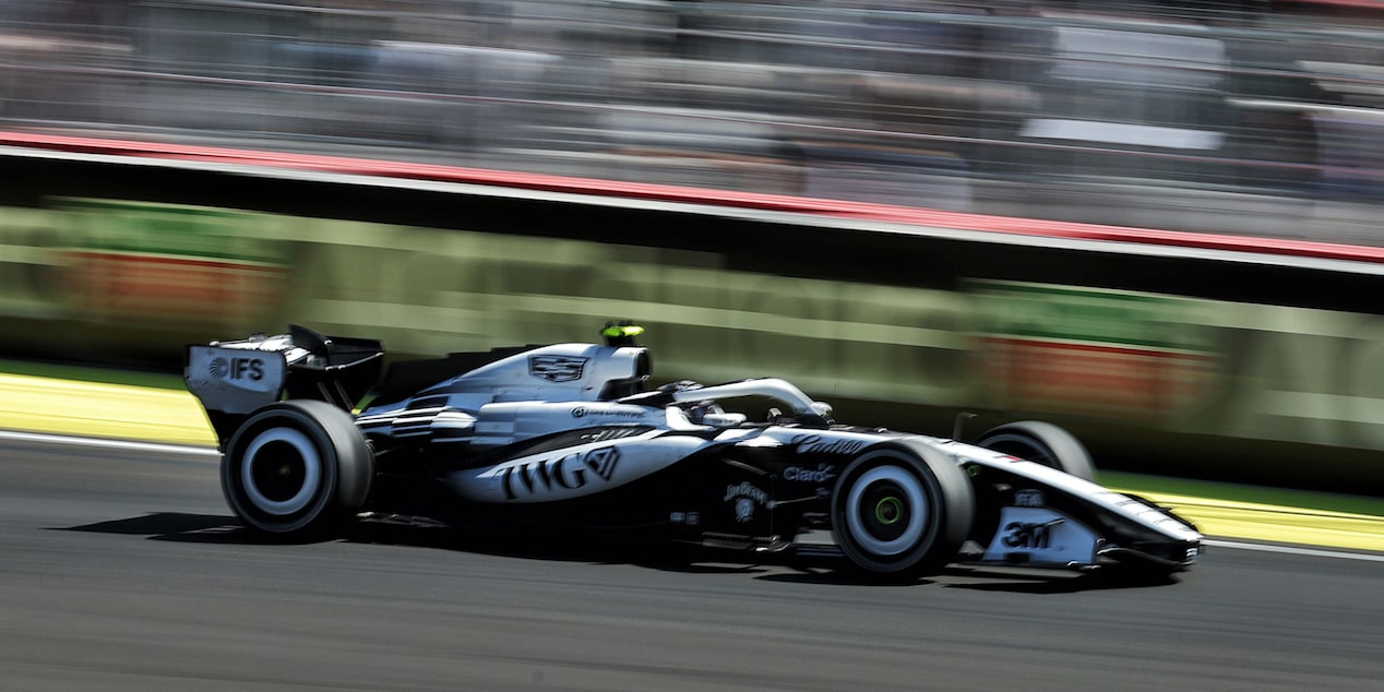 El auto de carrera Cadillac F1 de rines descubiertos avanza a toda velocidad por la pista durante la carrera. Desenfoque de movimiento de la multitud en el fondo.