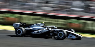El auto de carrera Cadillac F1 de rines descubiertos avanza a toda velocidad por la pista durante la carrera. Desenfoque de movimiento de la multitud en el fondo.