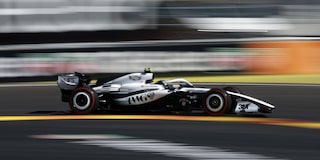 El auto de carrera Cadillac F1 de rines descubiertos toma una curva en el circuito durante la sesión de clasificación. Desenfoque de movimiento de la multitud en el fondo