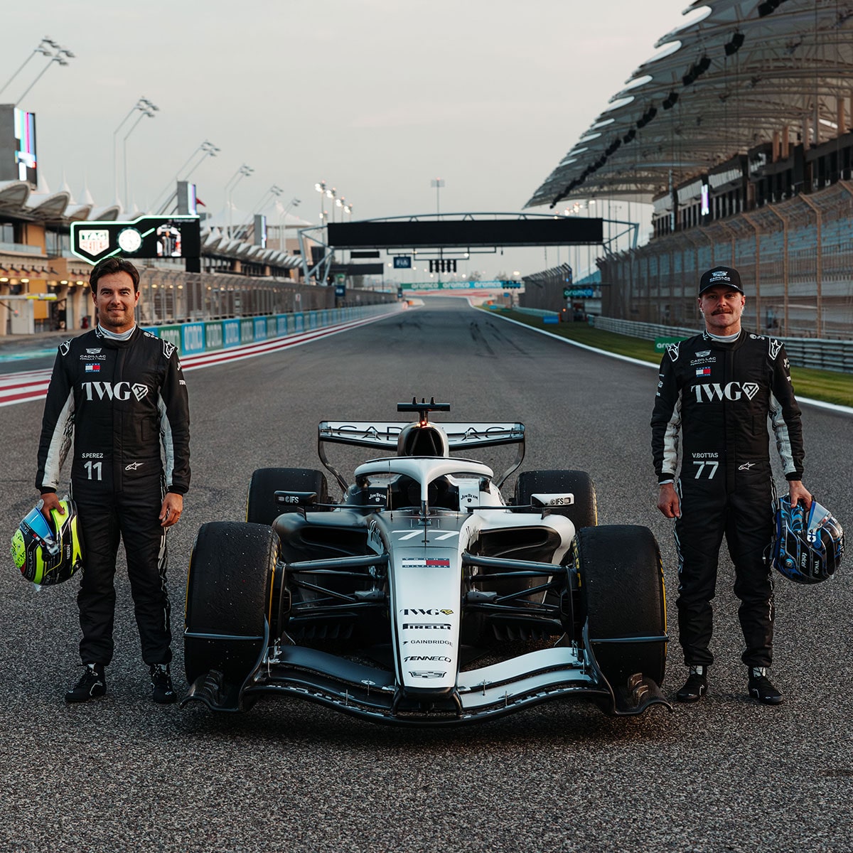 Two Cadillac F1 Team Drivers Posing Next to a Racecar Parked on the Track