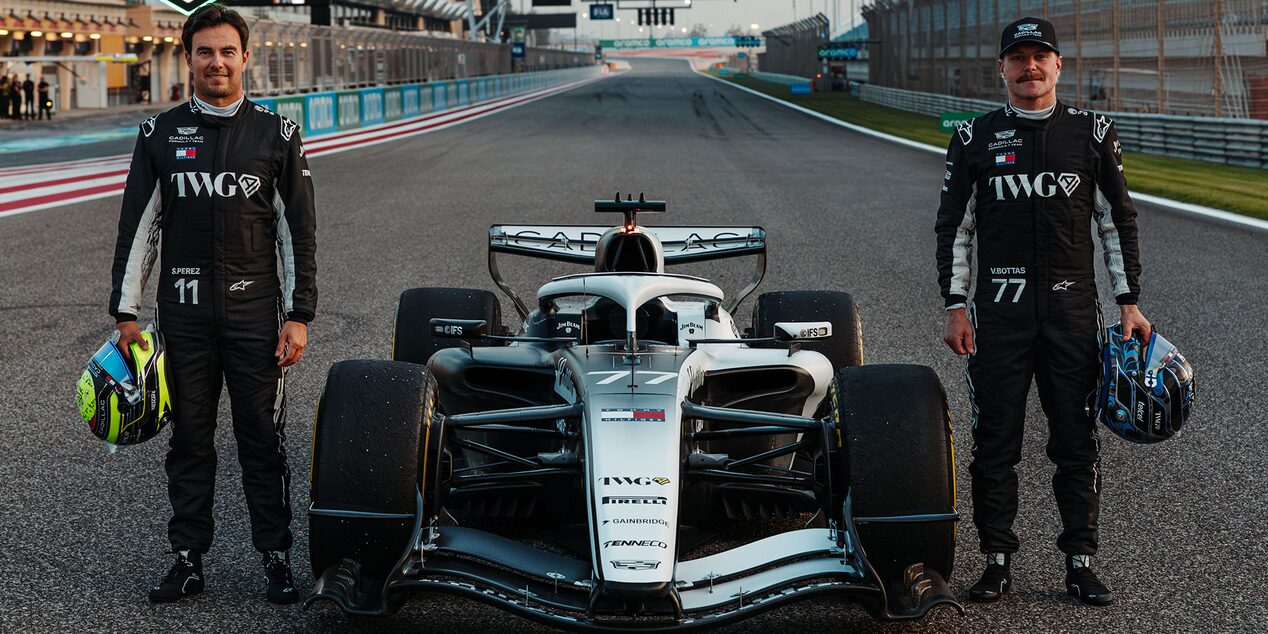Two Cadillac F1 Team Drivers Posing Next to a Racecar Parked on the Track