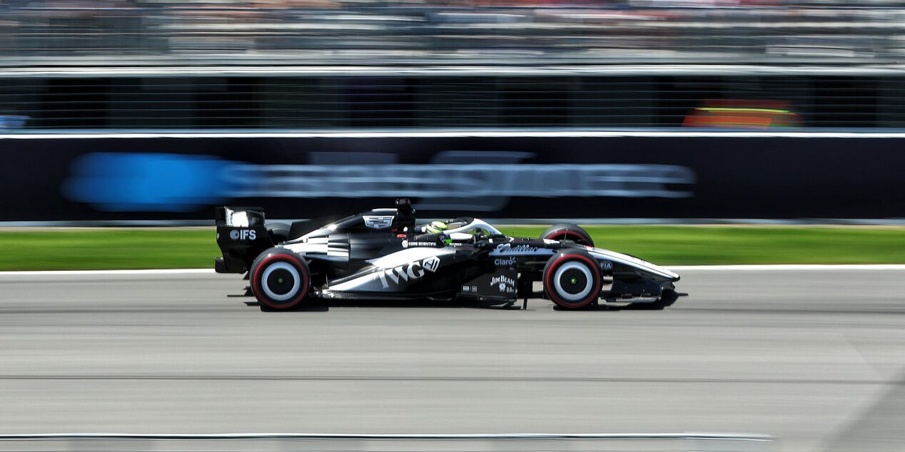 A Cadillac F1 Race Car Speeding Along a Track With Grandstands in the Background