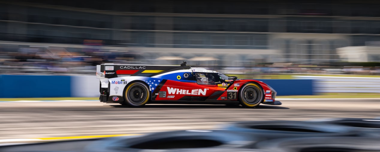 Four Happy Cadillac Race Car Drivers in Black and White Suits and Sunglasses Celebrating on a Podium With a Silver Trophy.