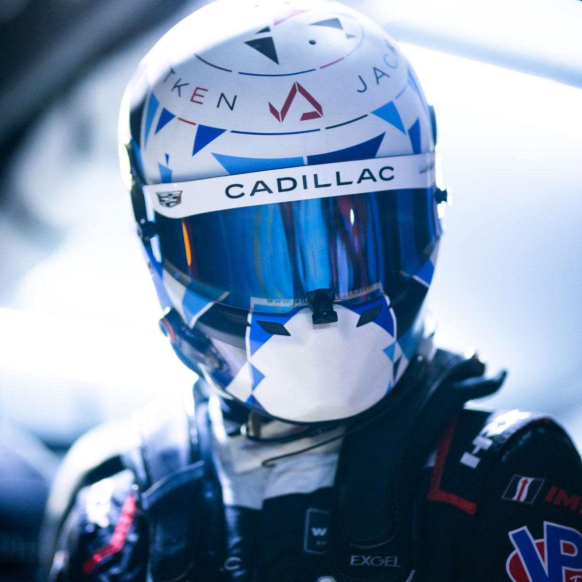 A Blue Cadillac V-Series.R Race Car Sits in the Pit Lane During a Stop as Crew Members Service the Vehicle Under Bright Daytime Light.