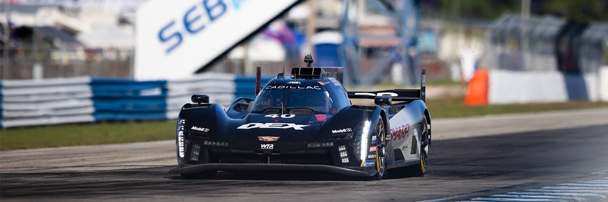 A Black Whelen Cadillac V-Series.R Race Car Drifts Through a Turn at Night With Its Headlights Casting Bright Beams Across the Track.