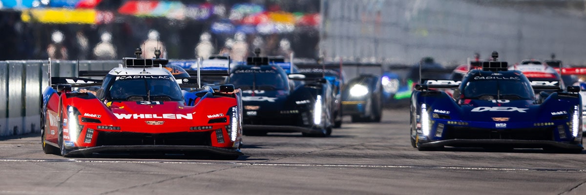 A Black Whelen Cadillac V-Series.R Race Car Drifts Through a Turn at Night With Its Headlights Casting Bright Beams Across the Track.