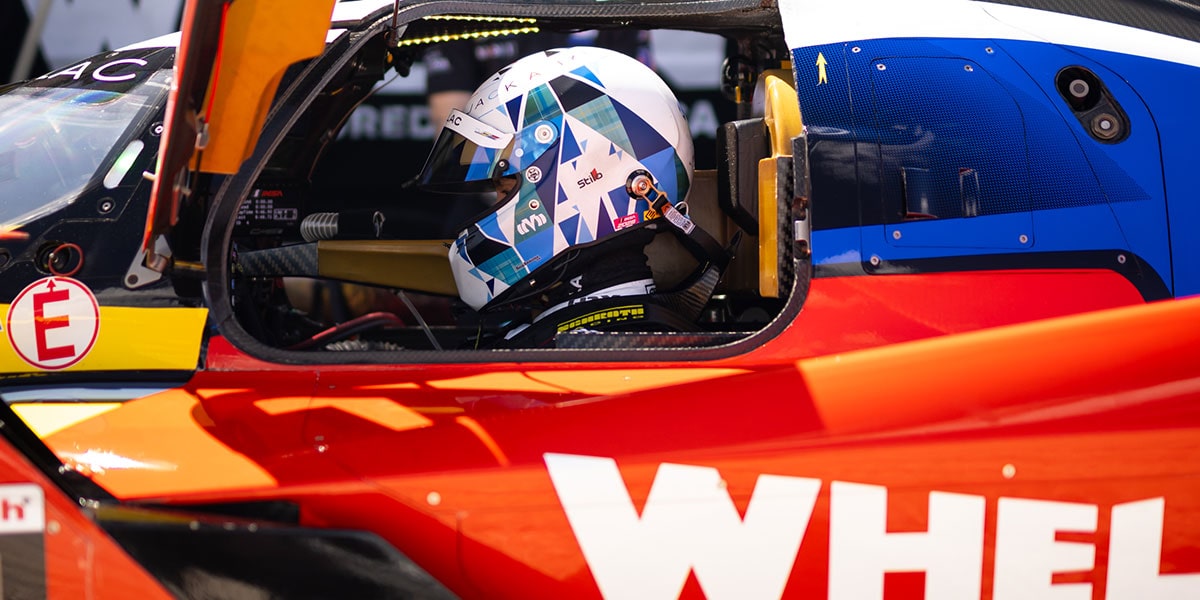 A Whelen Cadillac V-Series.R Race Car Enters the Pit Lane at Night With Intense Lights Illuminating the Front of the Vehicle and Crew Members Ready for Service.