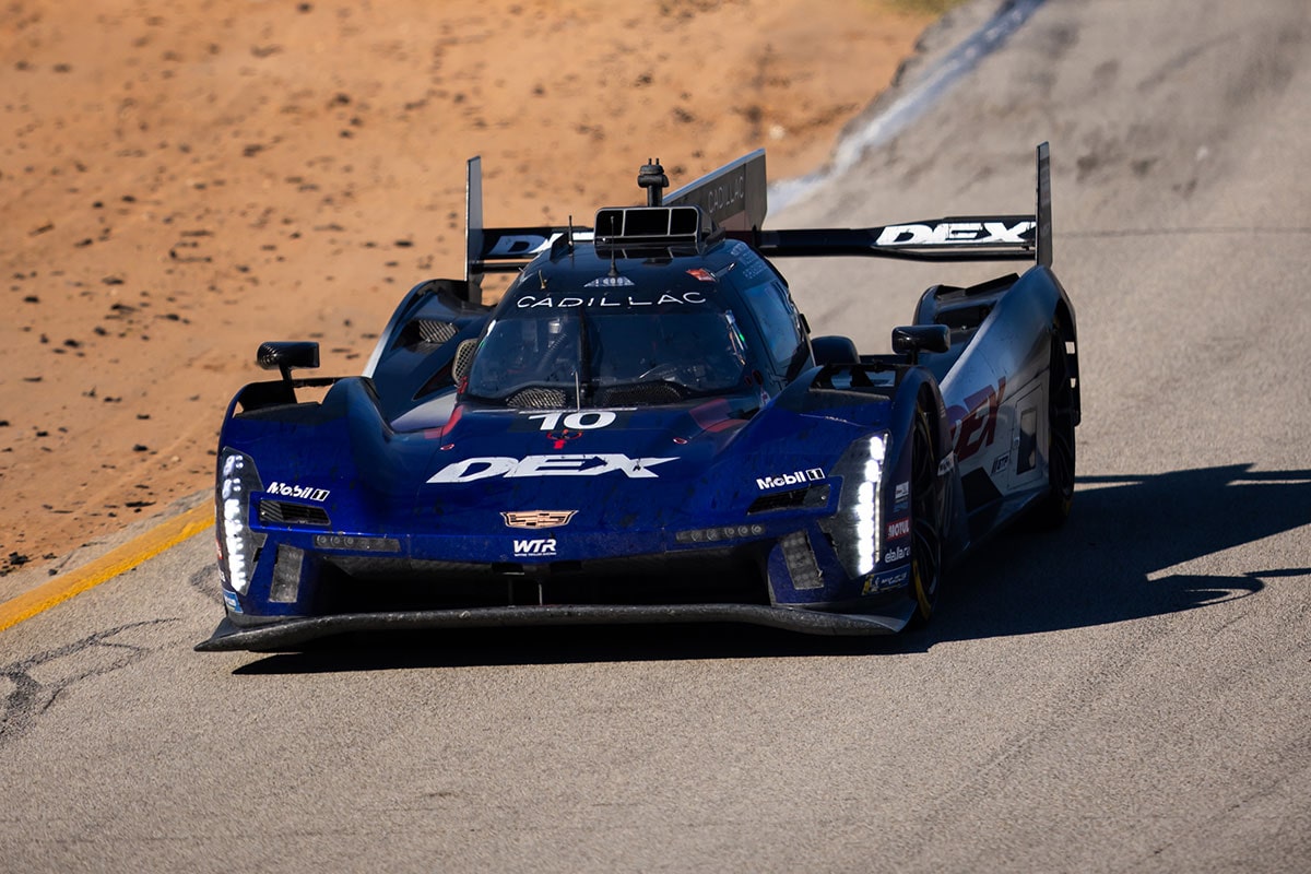 A Red Whelen Cadillac V-Series.R Race Car Speeds Down the Track at Night With Its Headlights Glowing and Motion Blur Emphasizing Its High Velocity.