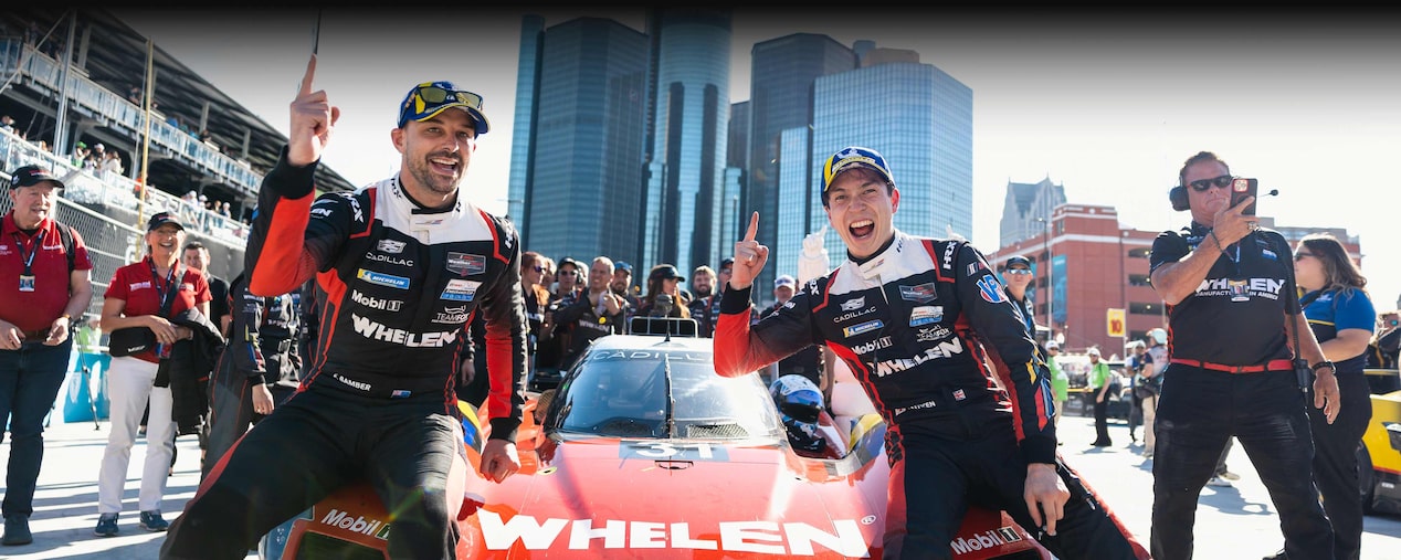 Four Happy Cadillac Race Car Drivers in Black and White Suits and Sunglasses Celebrating on a Podium With a Silver Trophy.