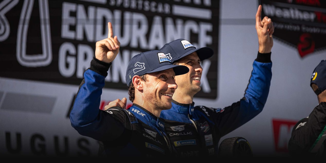 Tres pilotos del equipo Cadillac Racing, vestidos con trajes de carrera negros con la marca Whelen, de pie en un podio en Watkins Glen International sostienen trofeos de WeatherTech e IMSA frente a un fondo promocional con los logotipos del evento.