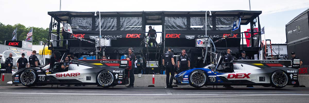 Un auto de carreras Cadillac azul y blanco con la marca DXC Technology circulando a gran velocidad, con efecto de desenfoque por movimiento, por una pista de superficie azul.