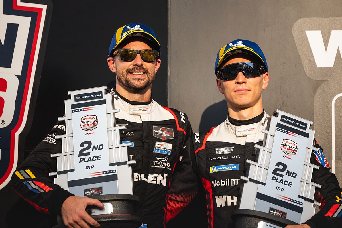 Two Cadillac Racing Drivers Hold Trophy Awards While Standing on a Podium Stage Following a Motorsports Competition.
