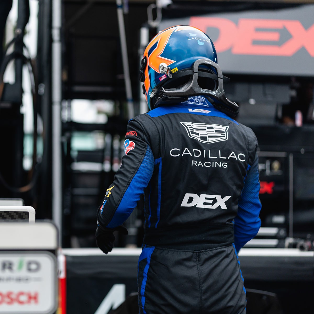 A Cadillac Racing Driver Wearing a Cadillac-Branded Racing Suit and Helmet Giving a Thumbs-Up