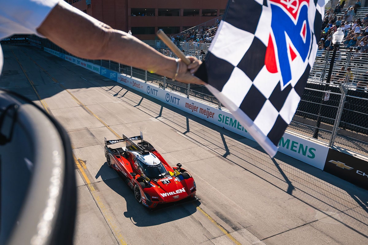 A Cadillac Racecar Driver Kneeling and Posing Next to a V-Series.R Racecar and a Sign Reading "IMSA Motul Pole Award 1 GTP"