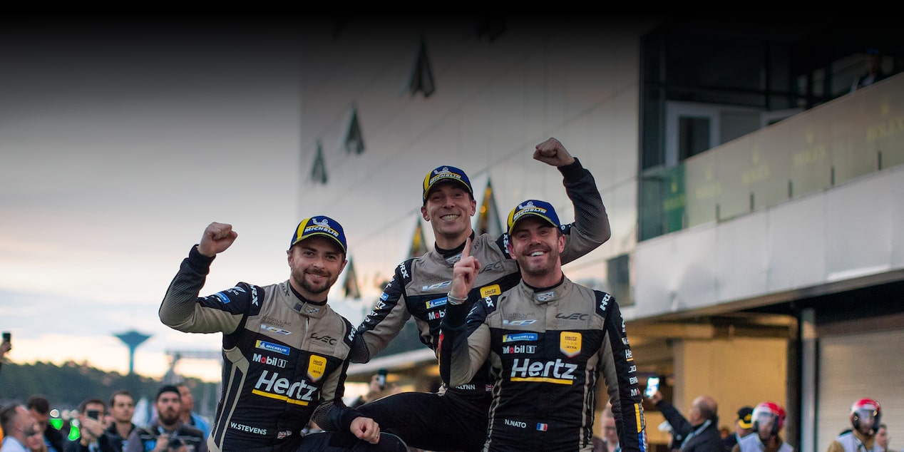 Three of the Cadillac Racing Team Members Smiling and Throwing Up a Number 1 and Their Fists Celebrating a Win