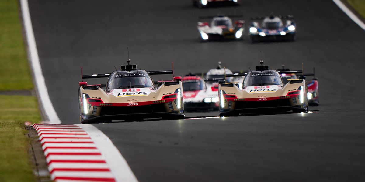 Two Pit Crew Members with a Tire and Drill Running Around the Front of the Cadillac V-Series.R Race Car