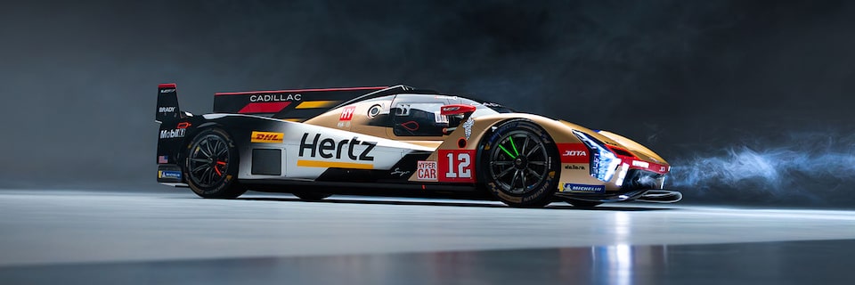 A Gold and Black Cadillac V-Series Race Car Number Twelve with Hertz Branding in a Smoky Studio Setting