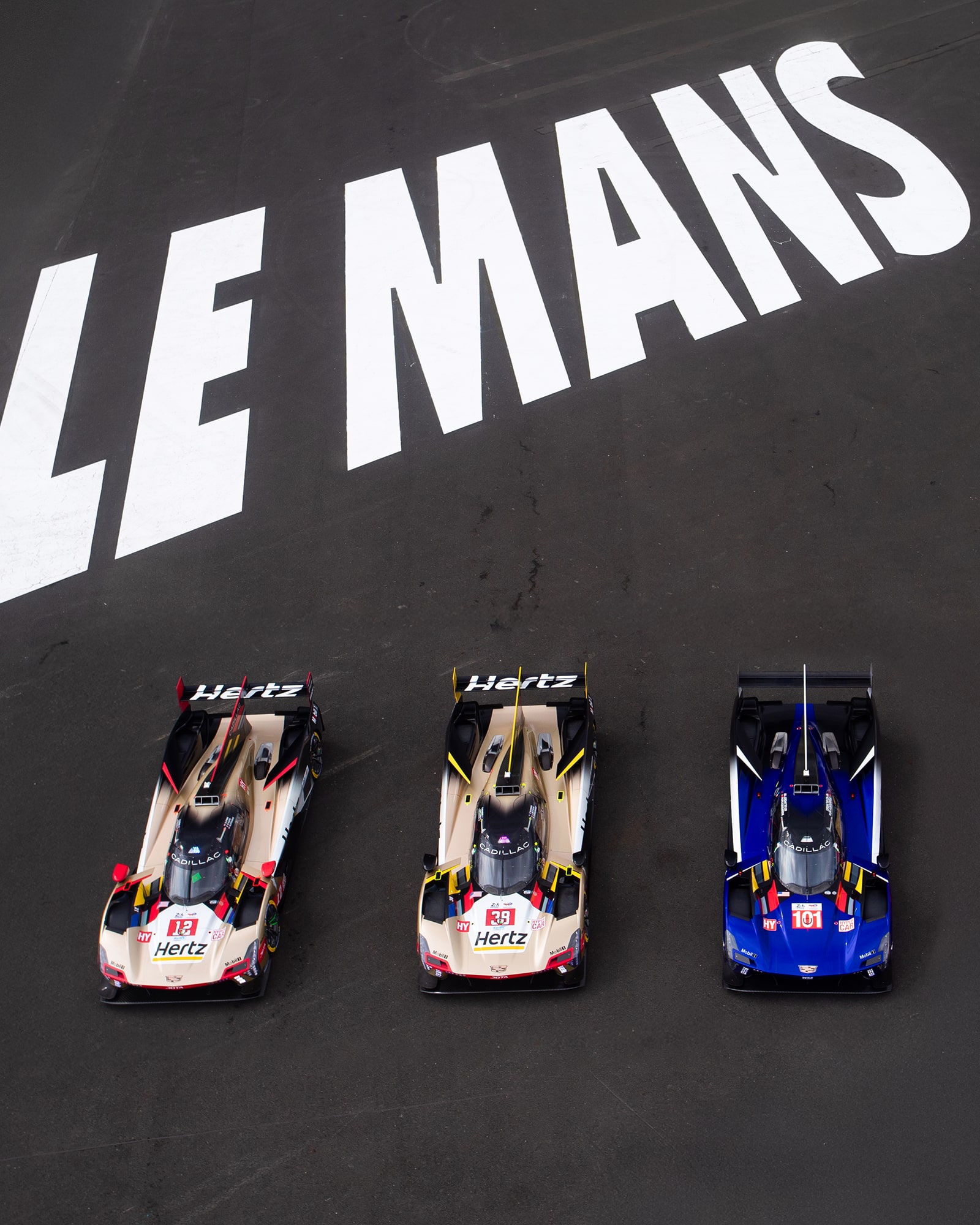 Two Gold and Red Cadillac Race Cars with Hertz Branding and One Blue and Red Cadillac Race Car Lined Up on the Le Mans Track