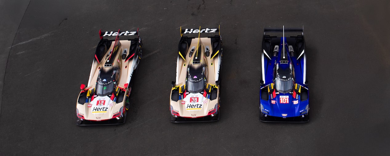 Two Gold and Red Cadillac Race Cars with Hertz Branding and One Blue and Red Cadillac Race Car Lined Up on the Le Mans Track