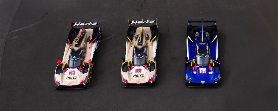 Two Gold and Red Cadillac Race Cars with Hertz Branding and One Blue and Red Cadillac Race Car Lined Up on the Le Mans Track