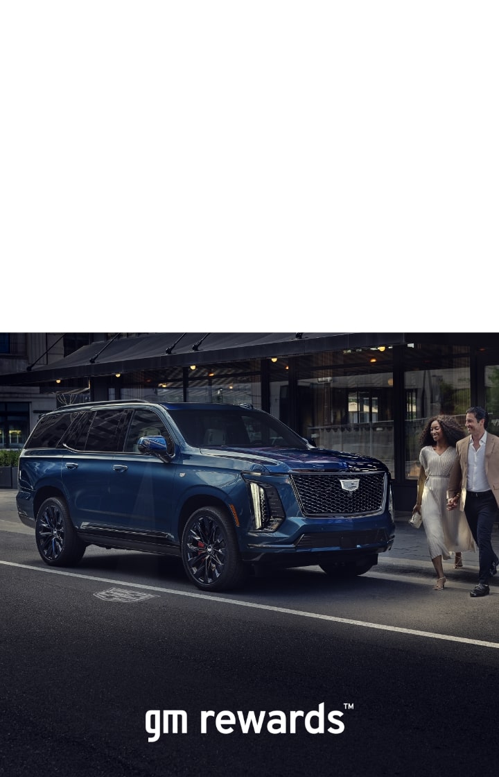 two people walking in front of a blue cadillac