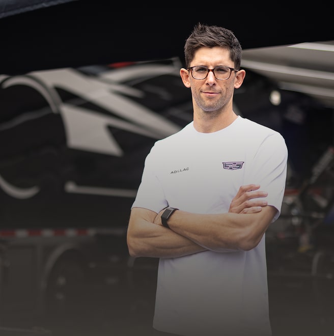 Man in glasses standing with arms folded in white Cadillac shirt