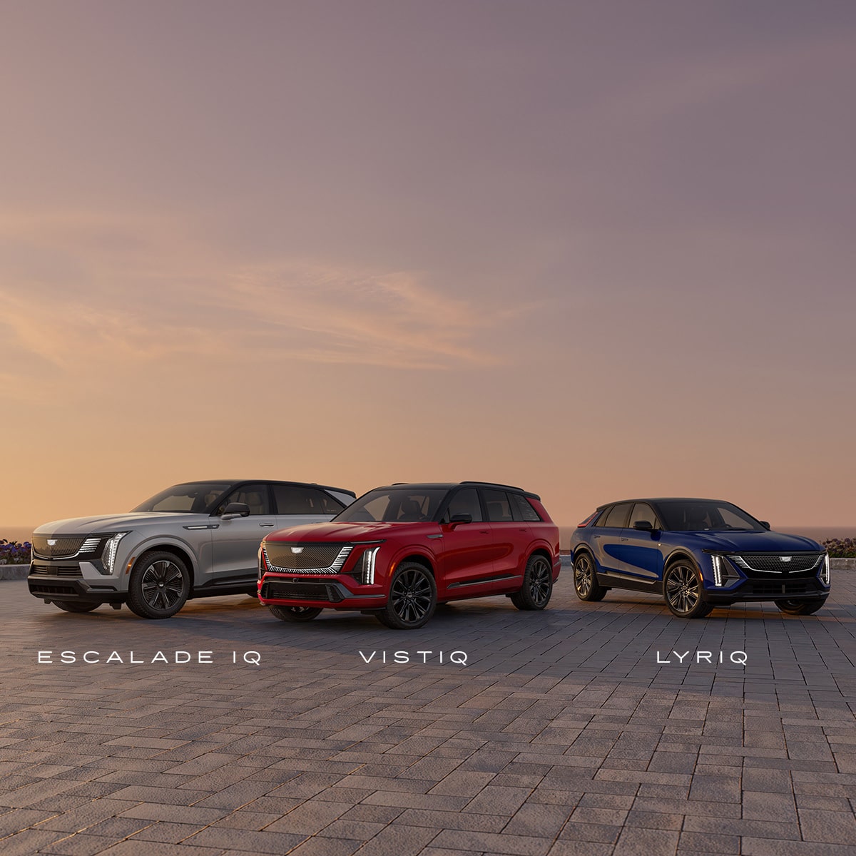 A Gray Cadillac Escalade IQ, a Red Cadillac Vistiq, and A Blue Cadillac OPTIQ Lined Up In A Sunset Background