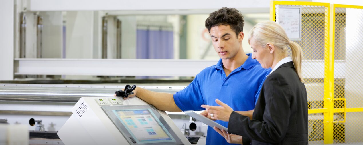 A man and woman standing over a computer in a factory.