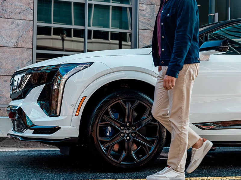 Hombre con gafas de sol elegantes y un traje azul sentado cómodamente en el asiento del copiloto de una Cadillac XT5