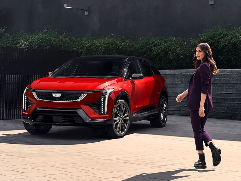 A Stylish Woman Walking Towards a Red Cadillac LYRIQ Parked in a Modern Courtyard
